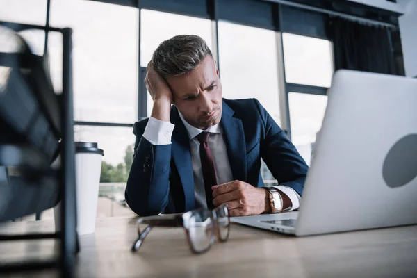 Selective focus of frustrated man looking at laptop in office — Stock Photo