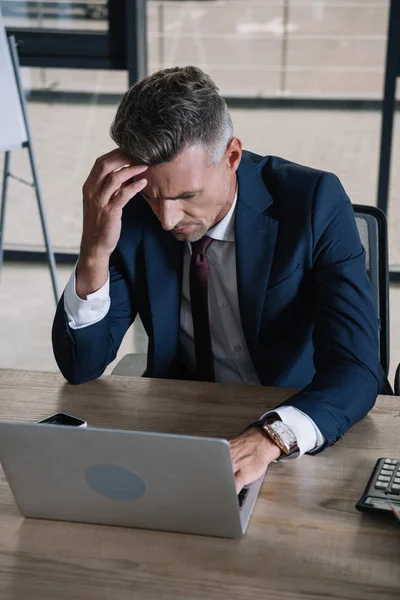 Hombre de negocios concentrado mirando el ordenador portátil mientras trabaja en la oficina - foto de stock