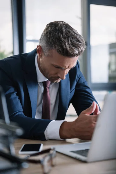 Enfoque selectivo de hombre de negocios sentado con las manos apretadas cerca de la computadora portátil - foto de stock