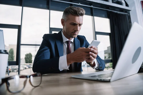 Enfoque selectivo del hombre utilizando el teléfono inteligente cerca de teléfonos inteligentes y gafas - foto de stock