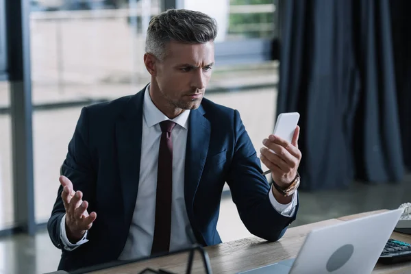 Selective focus of man in suit gesturing while looking at smartphone — Stock Photo