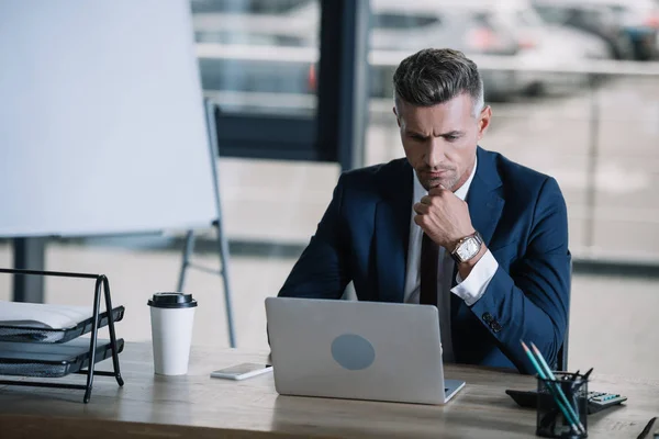 Hombre guapo mirando portátil cerca de teléfono inteligente en la mesa — Stock Photo