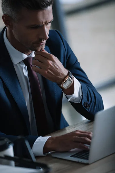 Selective focus of thoughtful businessman touching face while looking at laptop — Stock Photo