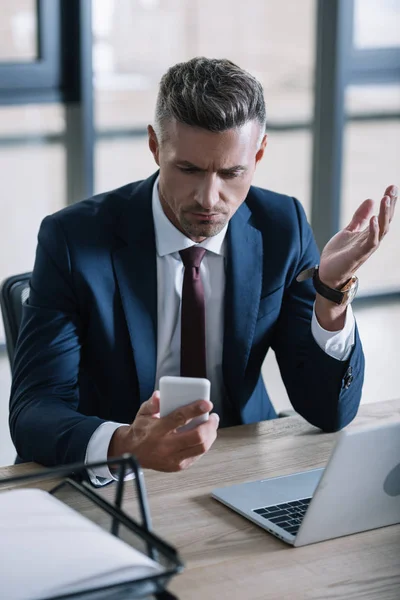 Selektiver Fokus des Geschäftsmannes gestikuliert beim Blick auf das Smartphone im Büro — Stockfoto