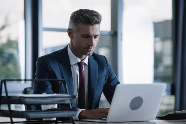 Foco seletivo do empresário bonito no desgaste formal usando laptop no escritório — Fotografia de Stock