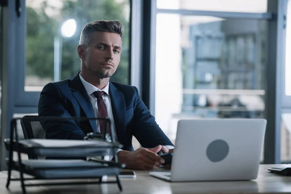 Foyer sélectif de l'homme assis près des gadgets près du plateau de documents dans le bureau — Photo de stock