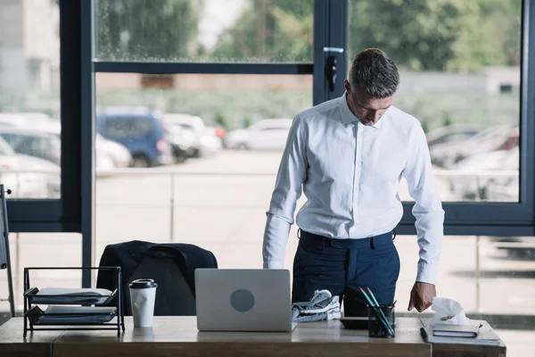 Bell'uomo d'affari in piedi vicino al computer portatile sulla scrivania in ufficio moderno — Foto stock