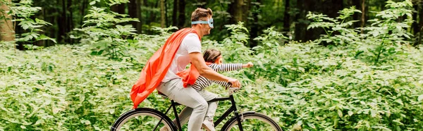 Panoramic shot of father and kid riding bicycle while boy looking forward — Stock Photo