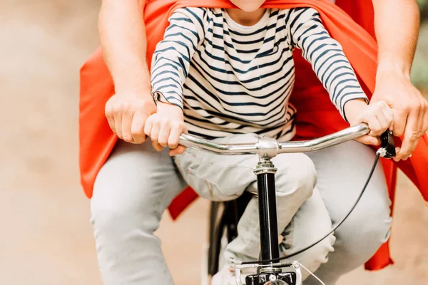 Vista recortada de padre con hijo capas rojas en bicicleta - foto de stock