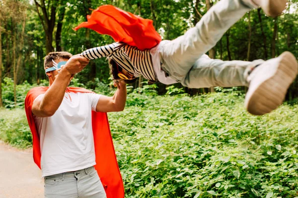 Vater in rotem Mantel dreht sich um Sohn in Superheldenkostüm und Maske — Stockfoto