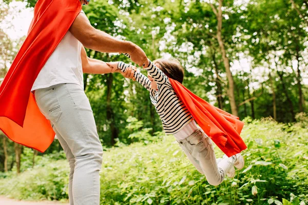 Cropped view of father spinning little boy in red superhero cloak — Stock Photo