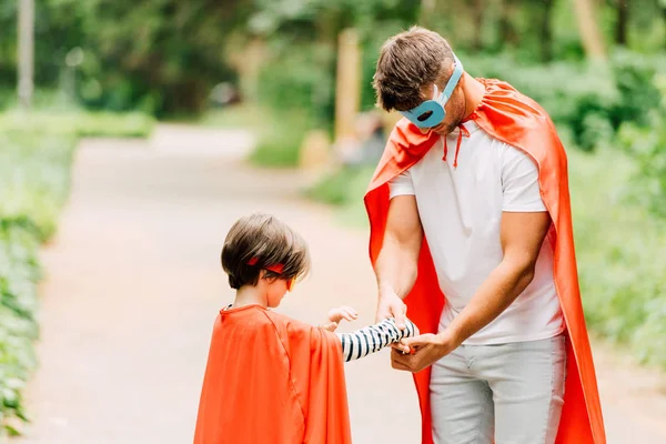 Father and son in superhero costumes standing on road while father holding hand of son — Stock Photo