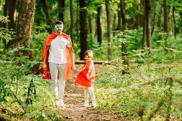 Vista completa de padre e hijo de pie en trajes de superhéroe en el bosque - foto de stock