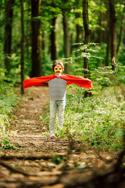 Foyer sélectif de petit garçon debout en costume de super-héros dans la forêt et — Photo de stock