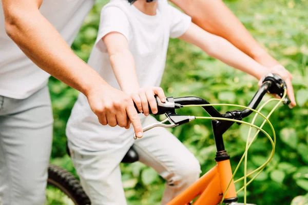 Vista recortada de padre e hijo sosteniendo asas de bicicleta mientras monta niño - foto de stock