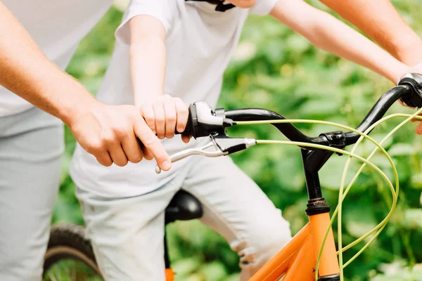 Cropped view of father holding brake on handle to help son riding — Stock Photo