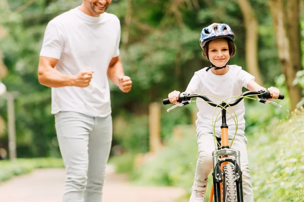 Vue recadrée du père fils acclamant tandis que le garçon à vélo et regardant la caméra — Photo de stock