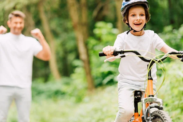 Messa a fuoco selettiva del padre tifo figlio mentre ragazzo in bicicletta e guardando la fotocamera — Foto stock