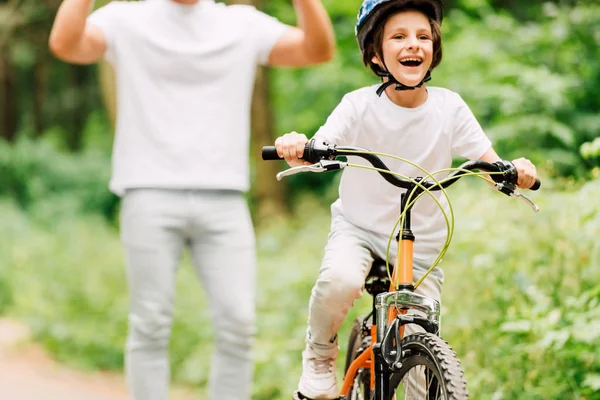 Recortado vista de aclamar hijo mientras niño montar en bicicleta y mirando hacia otro lado - foto de stock