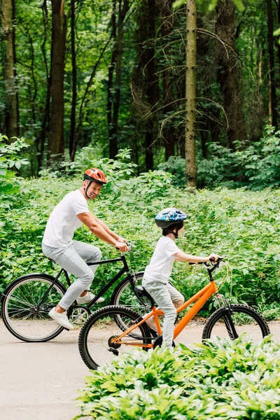 Ganzkörperansicht von Vater und Sohn beim Fahrradfahren, während Papa das Rad des Jungen betrachtet — Stockfoto