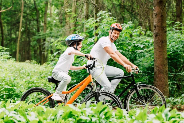 Счастливые отец и сын улыбаются во время езды на велосипеде — стоковое фото