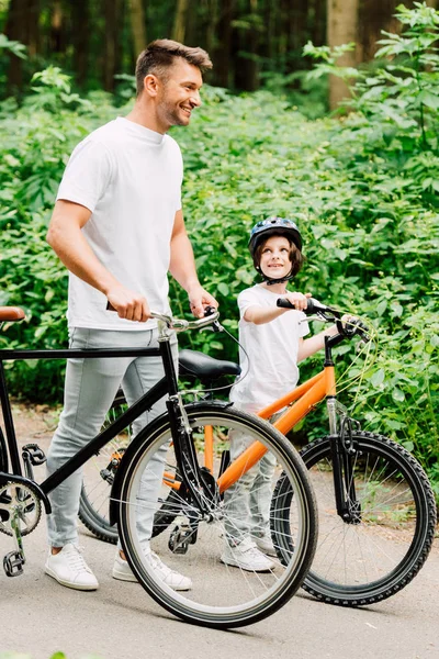 Pleine longueur vue de fahter et fils debout avec des vélos tandis que le garçon regardant papa — Photo de stock