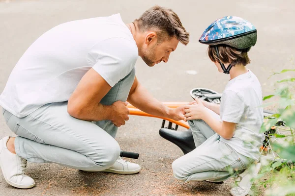 Father looking at knee of son because boy fell from bicycle — Stock Photo