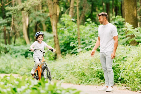 Pleine longueur vue de fils équitation vélo et père debout près de garçon et regardant enfant — Photo de stock