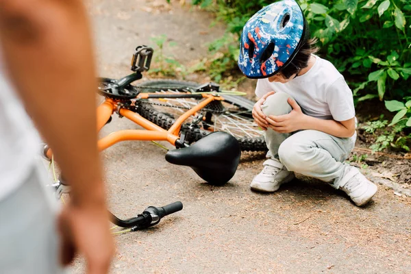 Enfoque selectivo del niño cayó de la bicicleta y mirando a la rodilla mientras el padre de pie cerca de su hijo - foto de stock