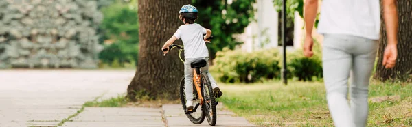 Panoramablick auf ein Kind, das Fahrrad fährt, während der Vater seinem Sohn hinterherläuft — Stockfoto
