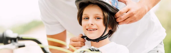Panoramic shot of happy son looking at camera while father putting helmet — Stock Photo