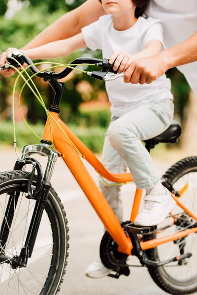 Cropped view of boy riding bicycle and father holding handles of bike to help son — Stock Photo