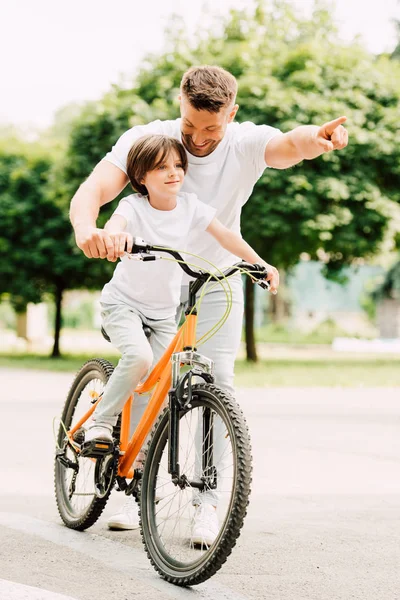Vista completa de la bicicleta de montar hijo mientras el padre señala con el dedo - foto de stock