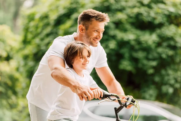 Selective focus of father and son holding handles of bicycle while looking forward — Stock Photo