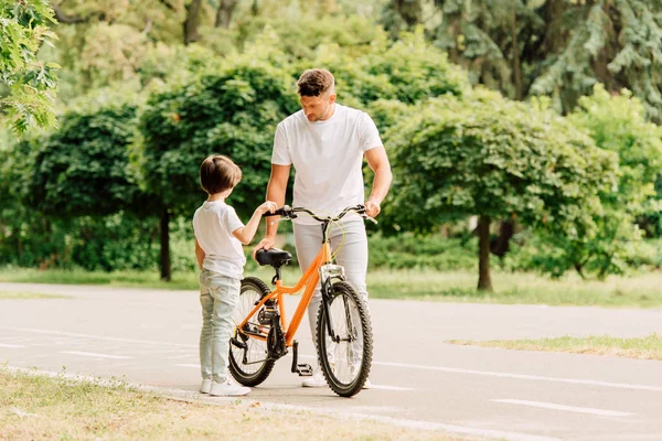 Повнометражний вид батька перевіряє велосипед, а син стоїть біля батька — стокове фото