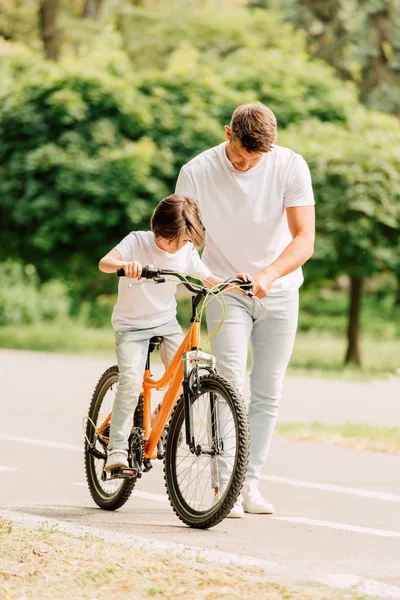 Full length view of father looking at son while kid riding bicycle — Stock Photo