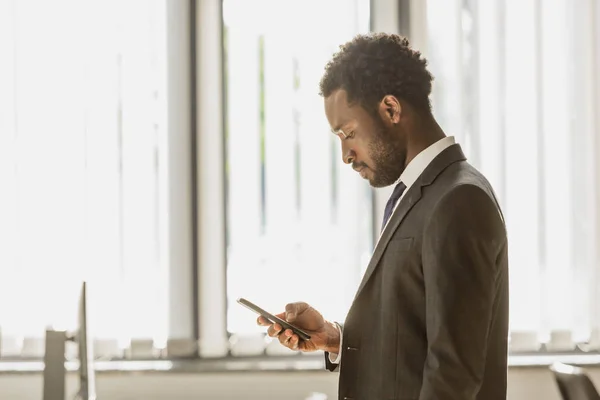 Pensativo empresário afro-americano usando smartphone no escritório — Fotografia de Stock