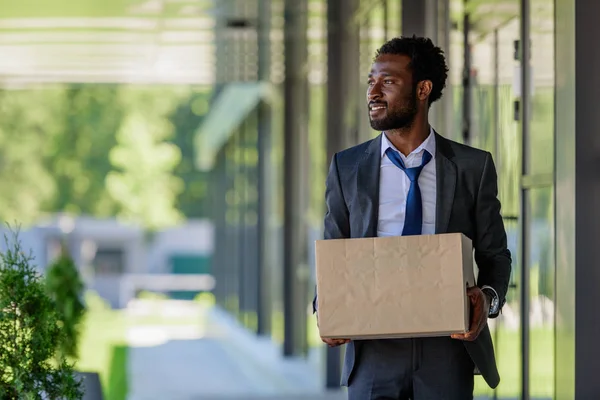 Nachdenklicher afrikanisch-amerikanischer Geschäftsmann schaut weg, während er einen Karton in der Hand hält — Stockfoto