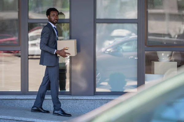 Selective focus of dismissed african american businessman carrying cardboard box — Stock Photo