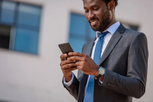 Alegre hombre de negocios afroamericano sonriendo mientras se utiliza el teléfono inteligente - foto de stock