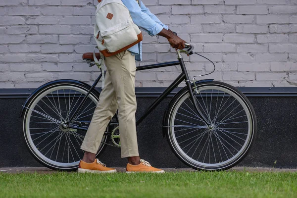 Vue recadrée de l'homme afro-américain debout avec vélo près du mur de briques — Photo de stock