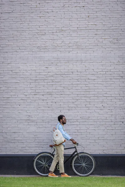 Стильний афроамериканський чоловік стоїть з велосипедом біля сірої цегляної стіни — стокове фото
