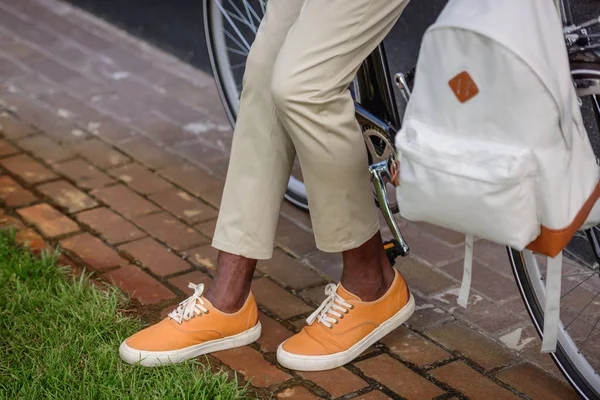 Vista cortada do homem americano africano elegante que está perto da bicicleta com mochila — Fotografia de Stock