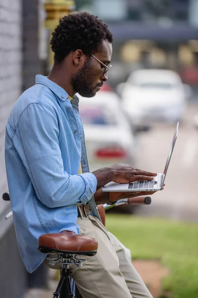 Schöner afrikanisch-amerikanischer Mann benutzt Laptop, während er in der Nähe von Fahrrad steht — Stockfoto