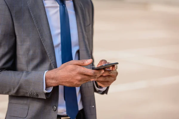 Vista recortada del hombre de negocios afroamericano en traje usando teléfono inteligente - foto de stock