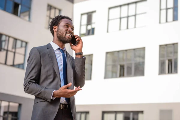 Fröhlicher afrikanisch-amerikanischer Mann gestikuliert und schaut weg, während er mit dem Smartphone spricht — Stockfoto