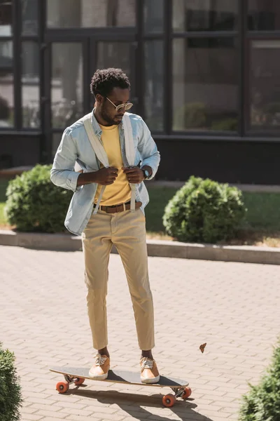 Handsome, stylish african american man riding longboard on sunny street — Stock Photo