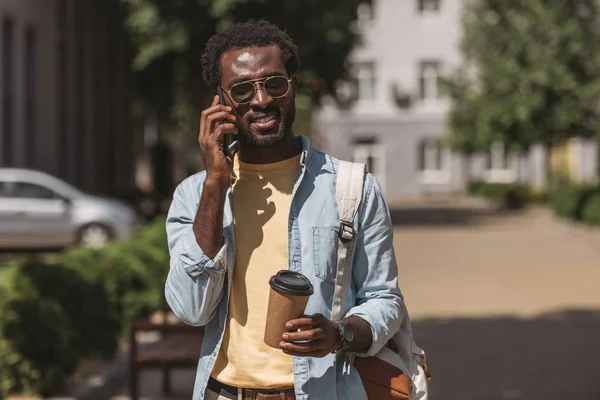 Homem americano africano elegante em óculos de sol falando no smartphone e segurando copo de papel — Fotografia de Stock