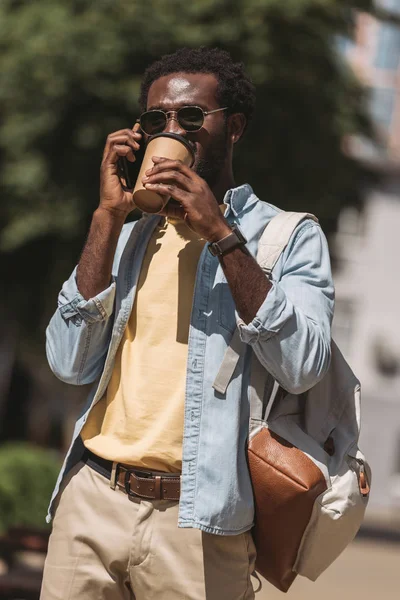 Bel homme afro-américain parlant sur smartphone et boire du café à partir d'une tasse jetable — Photo de stock