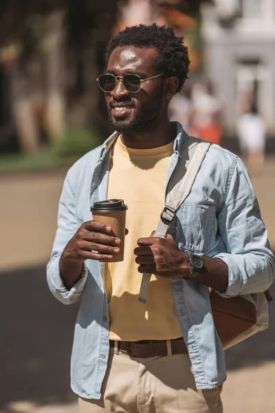 Hombre afroamericano elegante y alegre mirando hacia otro lado mientras sostiene la taza desechable - foto de stock